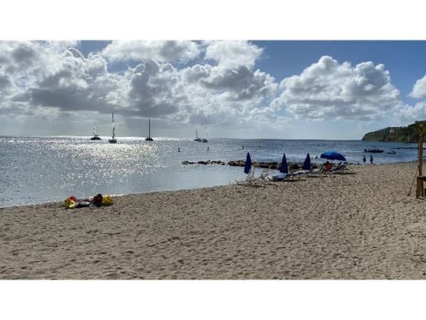 Sunny beach with lounge chairs and umbrellas by calm sea with sailboats.