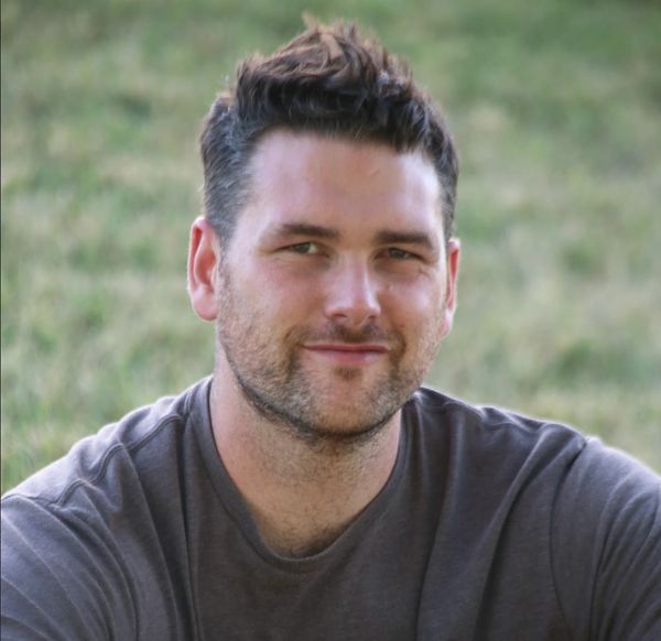 Smiling man with short hair and a beard outdoors.