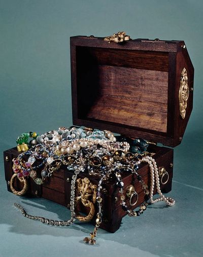 An open wooden chest overflowing with colorful jewelry and pearls.