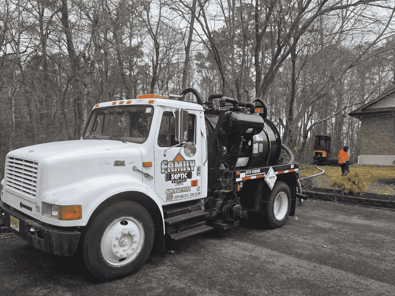 Septic service truck parked near a house with a worker in an orange jacket.