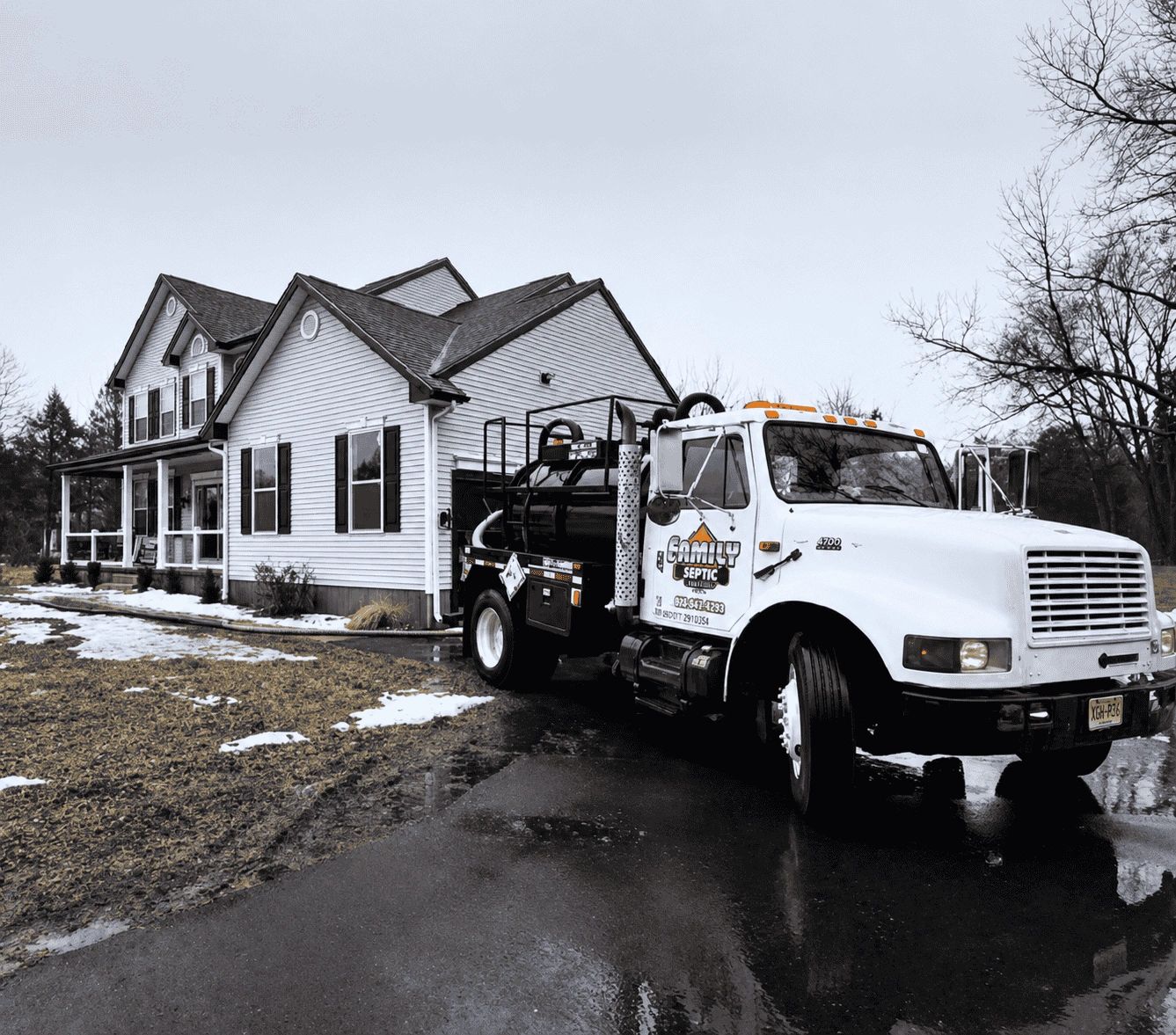 Septic service truck parked outside a suburban house on a wet day.