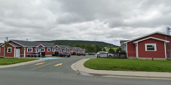 Row of red cottages with cars parked under a cloudy sky.