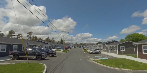A residential street with parked cars and single-story homes under a partly cloudy sky.
