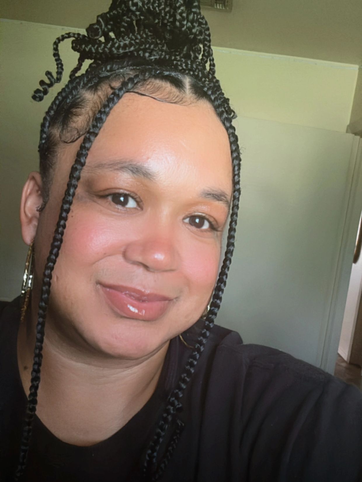 Woman with braided hair styled in a high bun, smiling warmly at the camera.