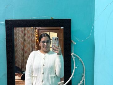 Young woman taking a mirror selfie in a cozy room with teal walls.