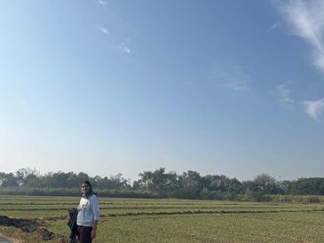 A person standing in a vast open field under a clear blue sky.