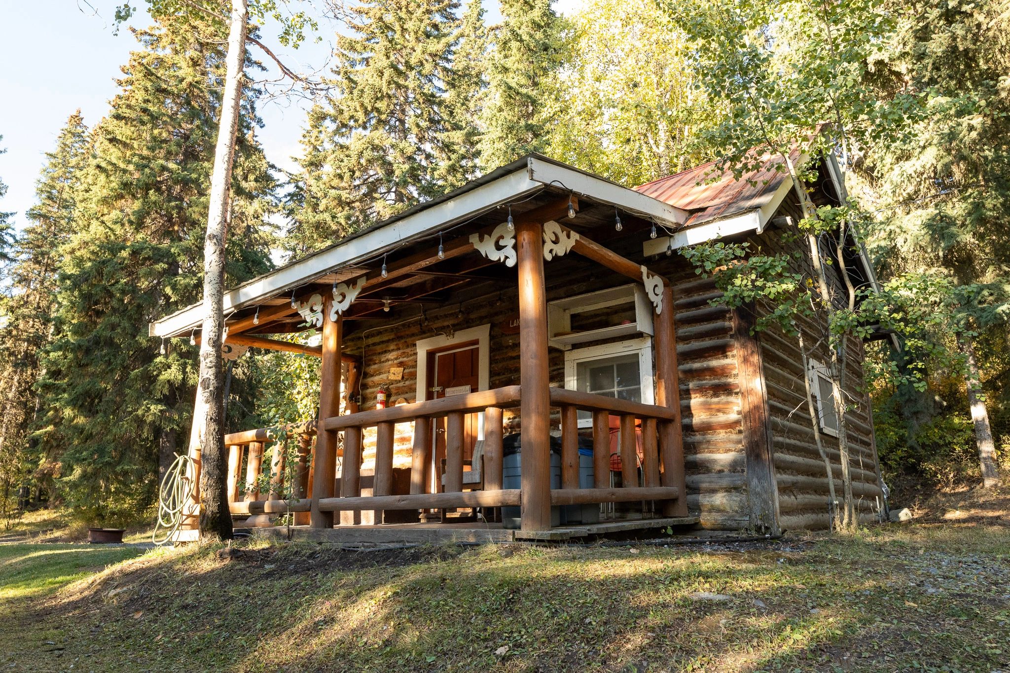 Rustic log cabin porch surrounded by trees in sunlight.