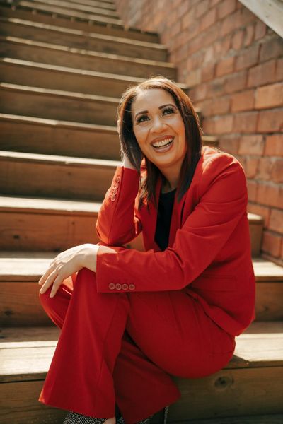 Woman in red suit smiling on wooden stairs.