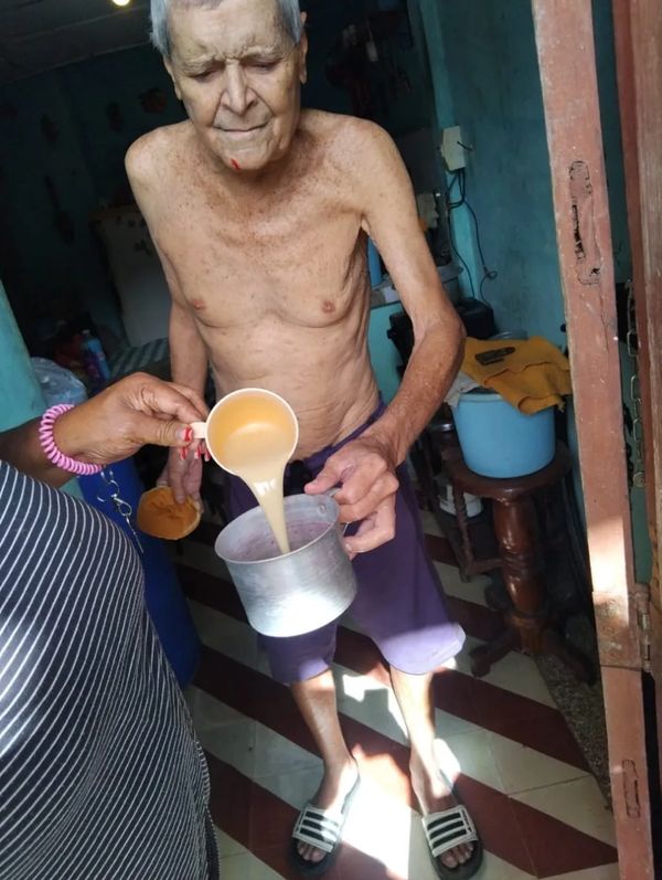 Elderly man being served a drink in a modest home setting.