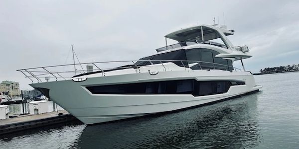 A sleek white yacht docked on calm water under a cloudy sky.