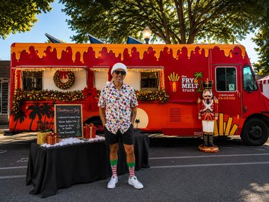 Man in festive outfit stands by a colorful food truck.