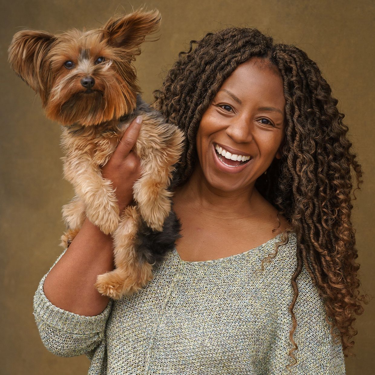 Smiling woman holding a small fluffy dog against a brown background.