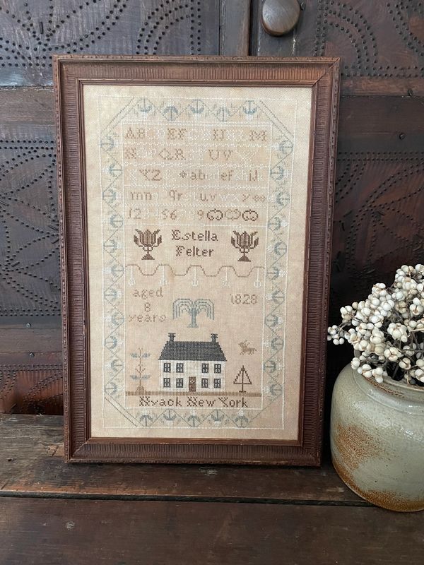 Reproduction cross stitch chart featuring a house and flowers and alphabet. 