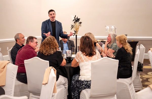 A man speaks to a group seated around a table at a formal event.