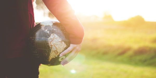 Person holding a globe outdoors with sunlight in the background.