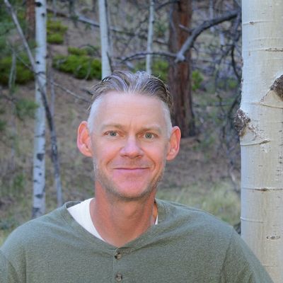 Man with short hair wearing a green shirt outdoors with trees.