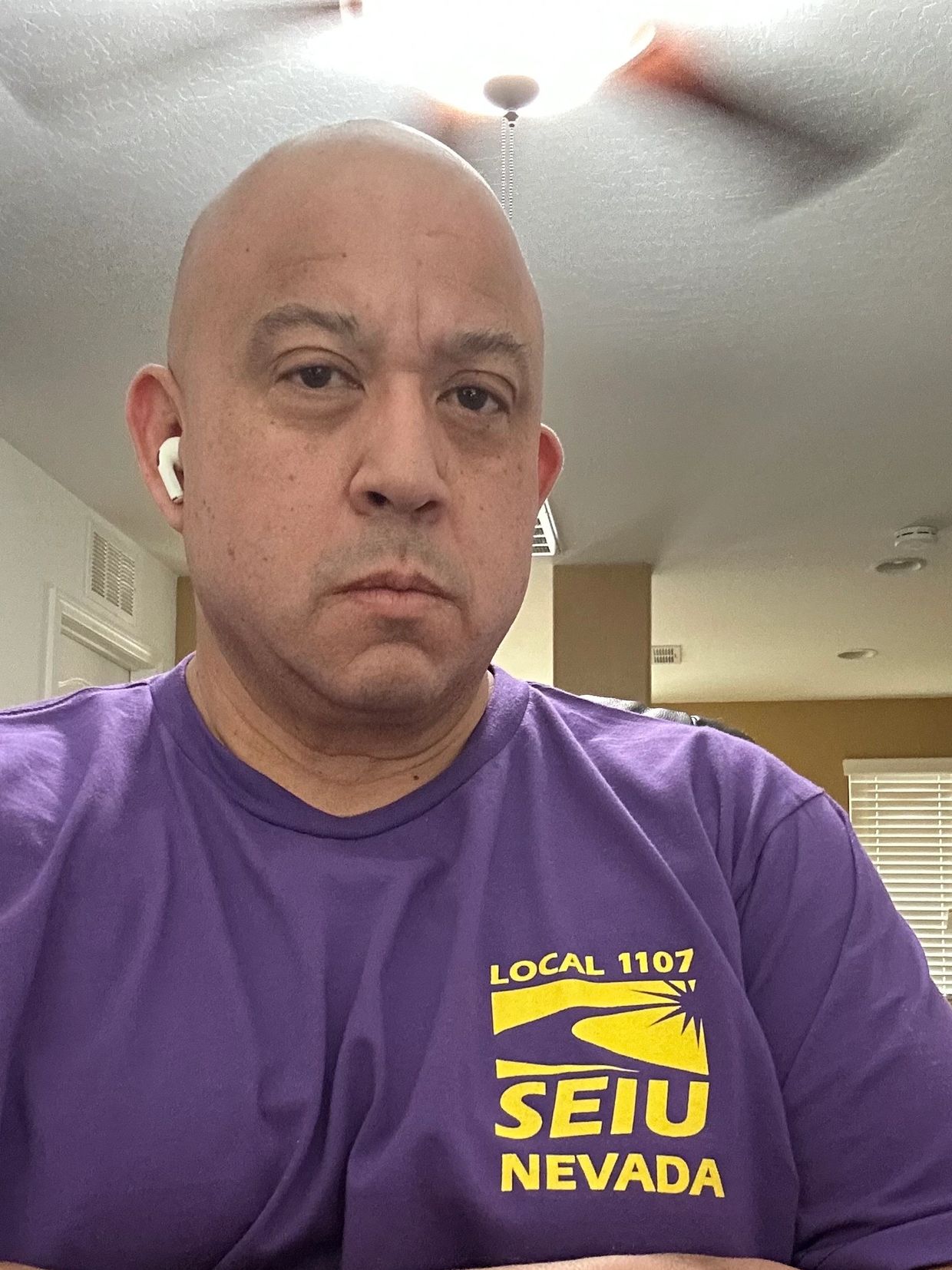 Man in a purple SEIU Nevada shirt with earbuds, indoors.