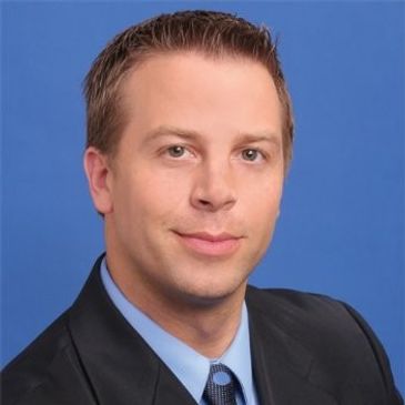 Professional headshot of a man in a suit against blue background.