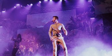 Performer singing on stage with purple lighting.