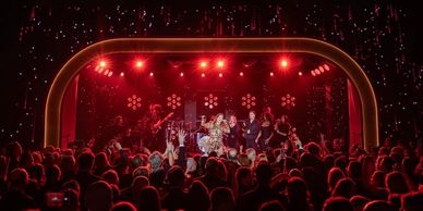 A lively concert with red stage lights and a cheering crowd.