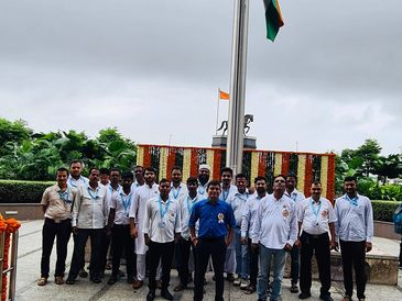 Group of men standing by the Indian flag on a cloudy day.