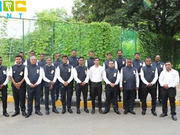 Group of men in formal attire posing outdoors with greenery in the background.