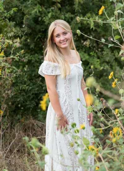 Senior portrait of a blonde graduate in a white dress surrounded by wildflowers in Central Texas.