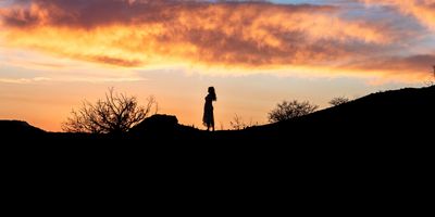 Silhouette of a person at sunset on a hill.