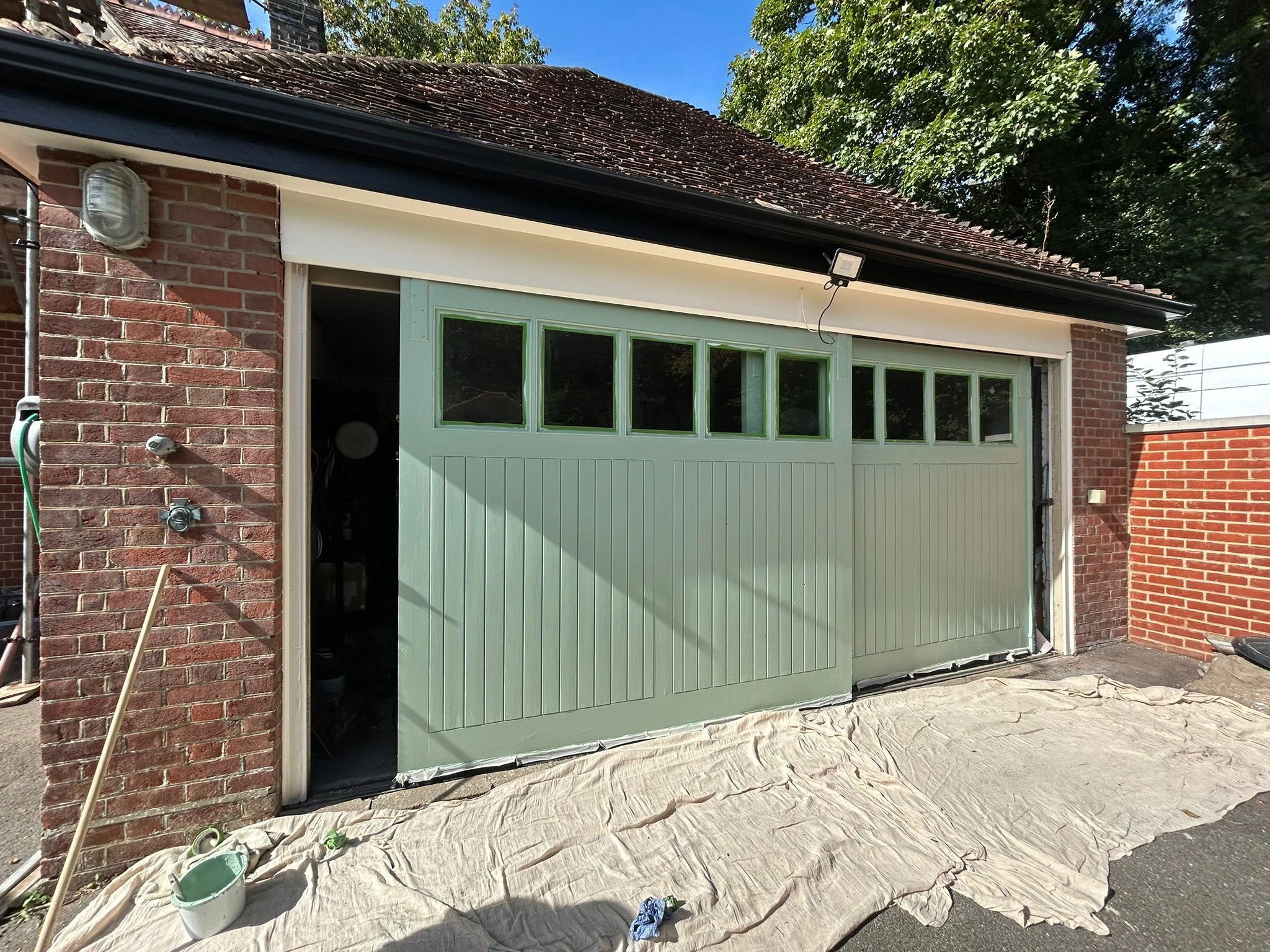 Freshly painted green garage doors with protective sheets on the ground.