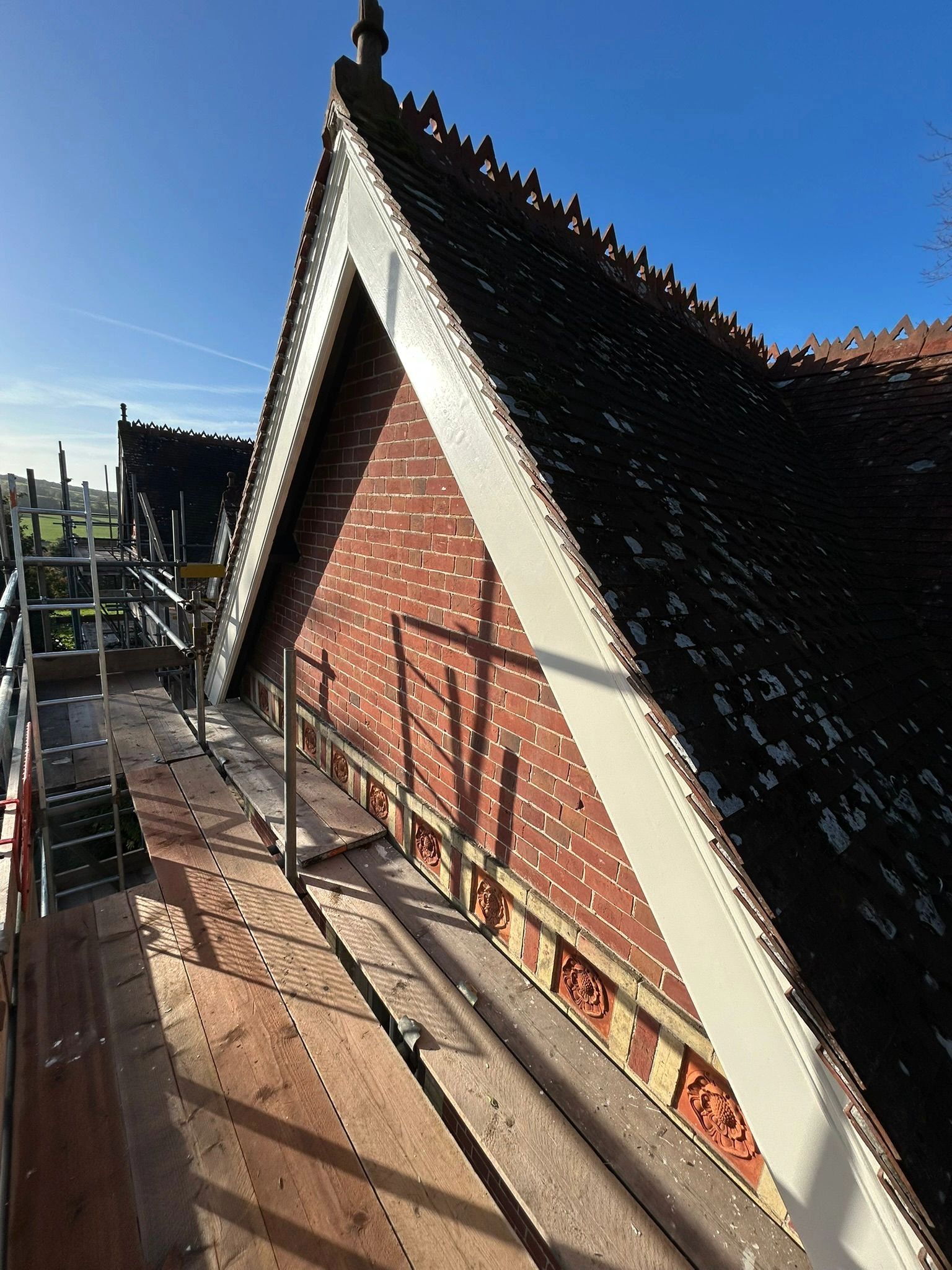 Scaffolding beside a brick gable roof under clear blue sky.