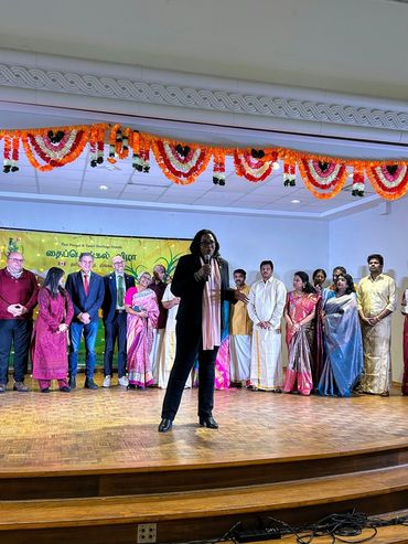 A speaker on stage with a group of traditionally dressed people behind.