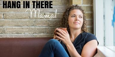 Woman sitting by a window with a cup, looking thoughtful.