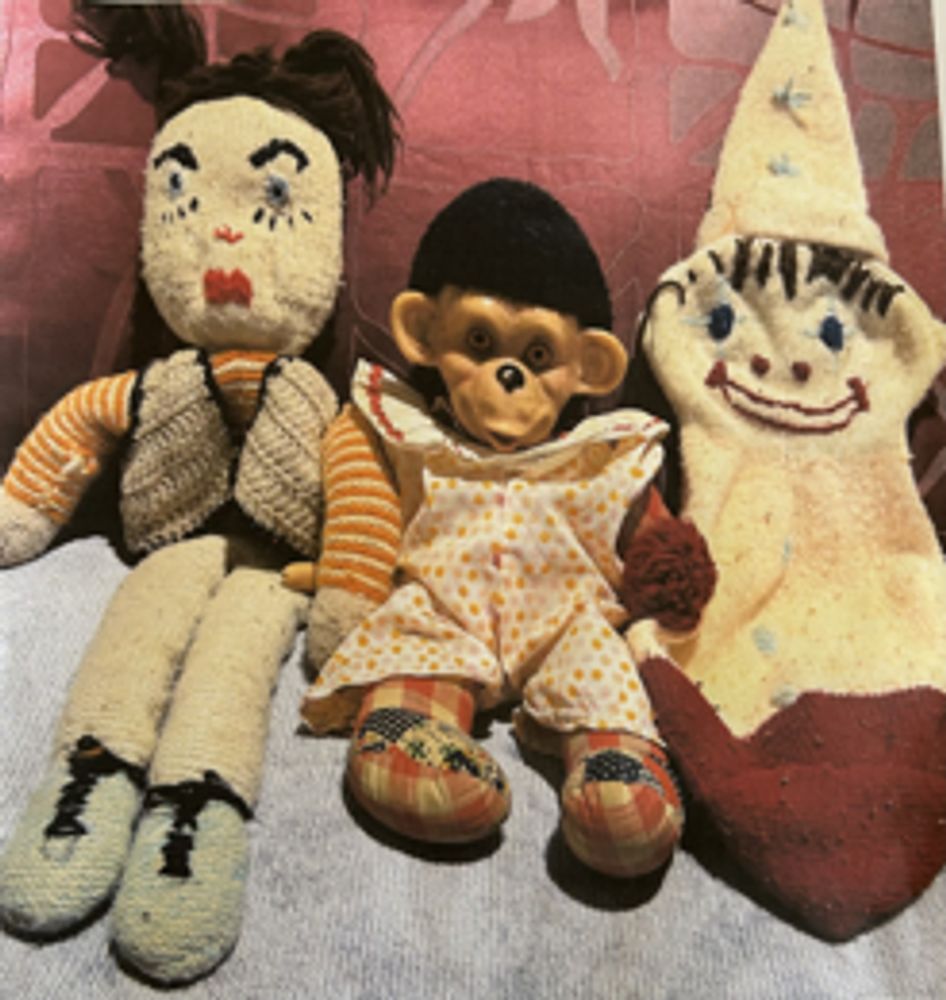 Three vintage dolls with distinct and quirky appearances on a fabric surface.
