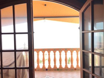 View through open glass doors to a sunlit balcony with terracotta tiles and balustrade.