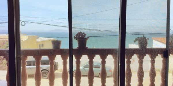 View of the ocean through a balcony with potted plants and parked cars.