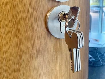 A set of keys inserted in a door lock on a wooden door.