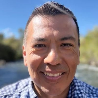 Man smiling outdoors near a river.