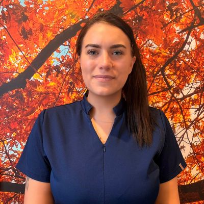 Woman in navy blue top poses in front of vibrant autumn leaves.