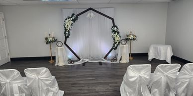 Elegant indoor wedding setup with white decorations and floral arch.