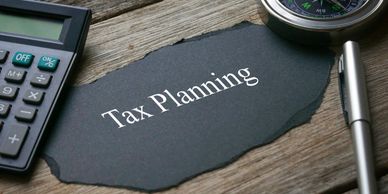 Compass,calculator,pen and a piece of black paper written with Tax Planning on wooden background.