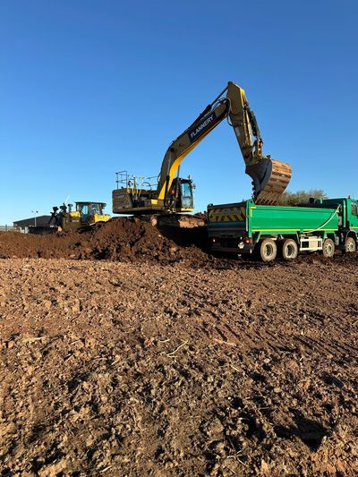 Excavator loading soil into green truck on a construction site.
