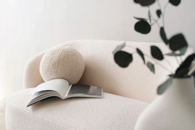 White boucle couch with round pillow and book sitting on top and a few leaves to the right corner.
