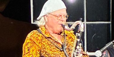 Musician playing saxophone wearing a white cap and patterned shirt.
