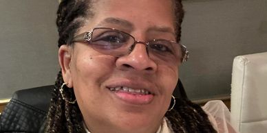 Smiling woman with braided hair and glasses indoors.