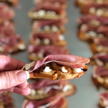 Hand holding a cracker with meat and cream cheese.