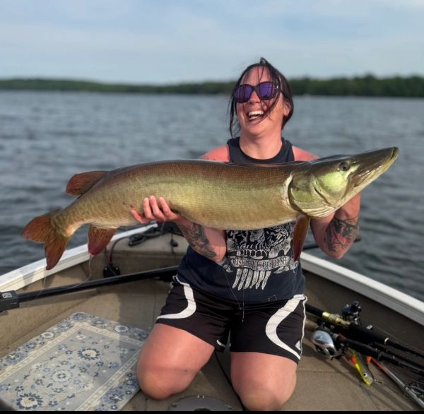 Woman proudly holds a large fish on a boat.