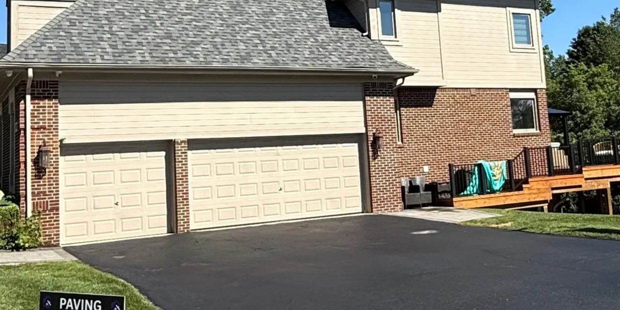 Freshly paved driveway in front of a brick house with beige garage doors.