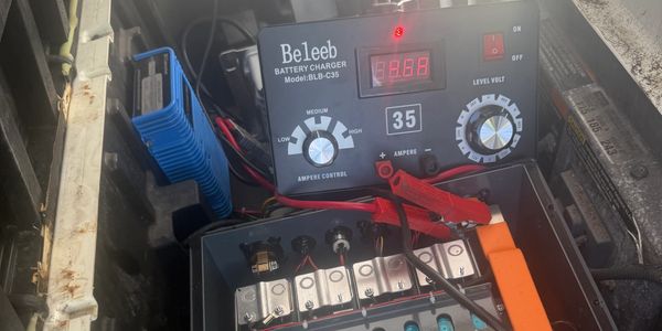 Beleeb battery charger connected to a car battery inside an engine compartment.
