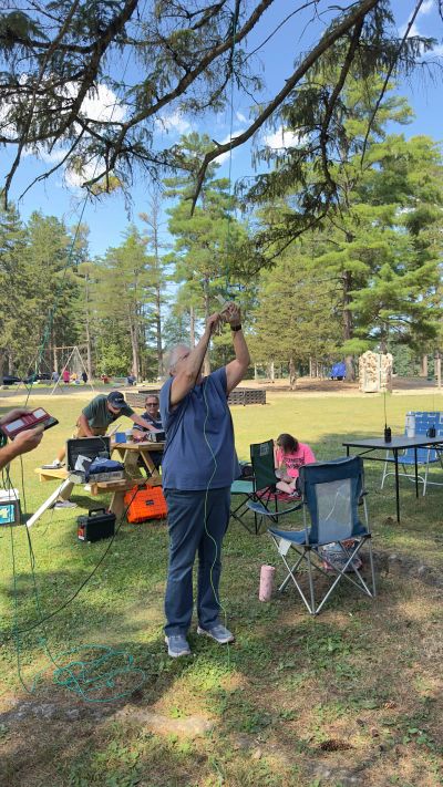 Person setting up equipment outdoors with others nearby.