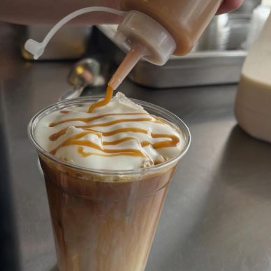 Iced coffee being topped with caramel drizzle.